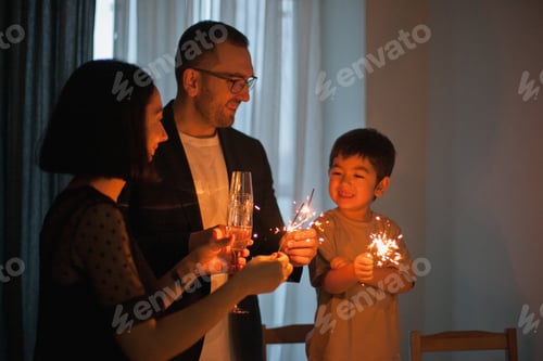 Visualização: Família feliz comemorando a véspera de ano novo em casa com estrelinhas e velas à noite na cozinha