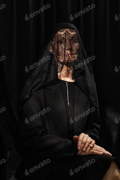 Preview: Senior Woman in Lace Veil Covering Face Sitting on Black Background in Studio