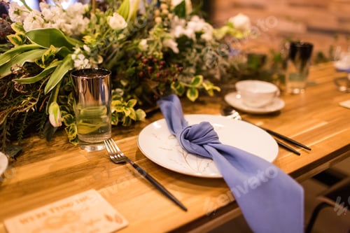 Preview: Closeup shot of a plate on the table with glasses and bouquets under the lights in a restaurant