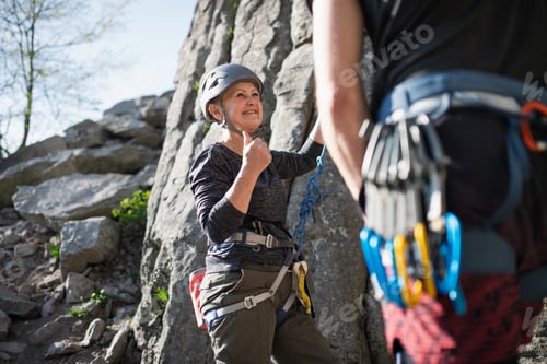 Preview: Senior woman with instructor climbing rocks outdoors in nature, active lifestyle