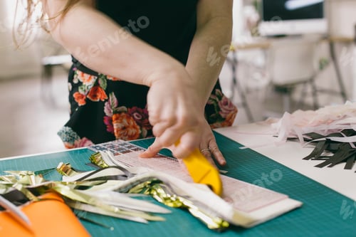 Preview: Close up of female textile designer cutting textiles in design studio