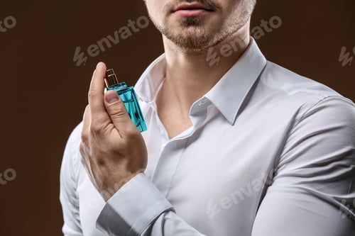 Preview: Handsome man in shirt using perfume on dark background, closeup