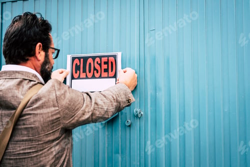 Preview: Failed business man store owner with closed signs on the door of his shop - coronavirus lockdown