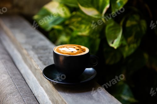 Preview: Black mug of cappuccino with latte art on wooden background with tropical plants