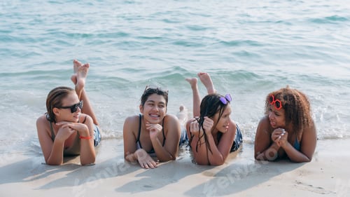 Preview: Teenagers laughing and playing in the sea with colorful swim rings, enjoying youthful summer fun.