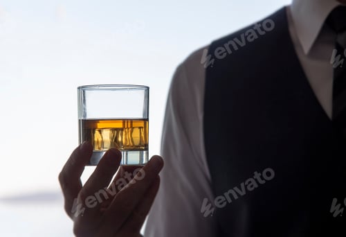 Preview: Whiskey on ice drink glass in silhouetted hand at social gathering.