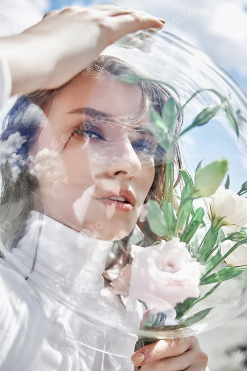Preview: Woman with a round aquarium on her head holds flowers near her face. Concept of a girl cosmonaut
