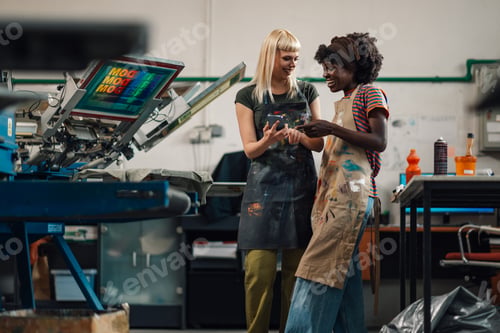 Preview: Interracial female graphic technicians smiling at phone at facility.