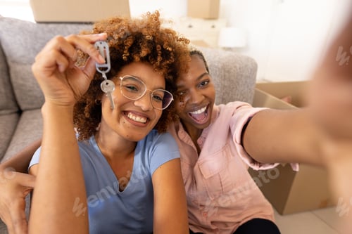 Preview: Multiracial lesbian couple screaming and smiling while showing new house key by sofa at home