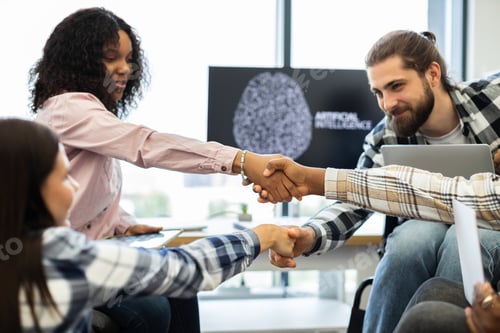 Preview: Diverse team celebrates success with a handshake in a tech environment