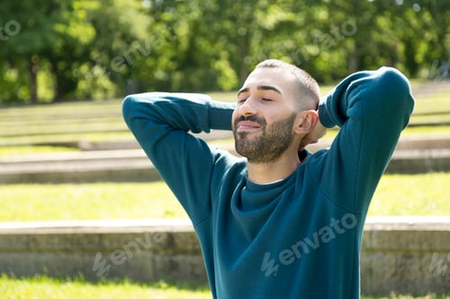 Preview: Relaxed young Caucasian man with hands behind his neck, enjoying leisure time in a natural park