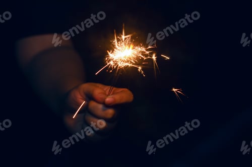 Preview: Woman hand holding a burning sparkler. Christmas and new year sparkler holiday background