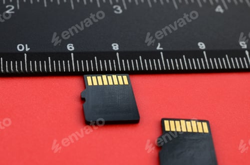 Preview: Two small micro SD memory cards lie on a red background next to a black ruler