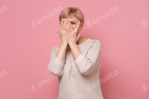 Preview: Woman Peeking Through Fingers Against Pink Background