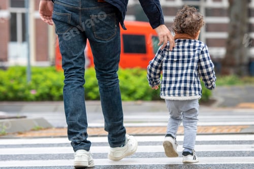 Preview: A parent and child holding hands crossing the street together.