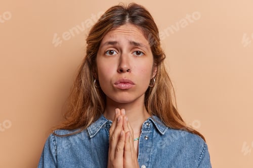 Preview: Photo of displeased young European woman begging for something holding hands folded in prayer pose