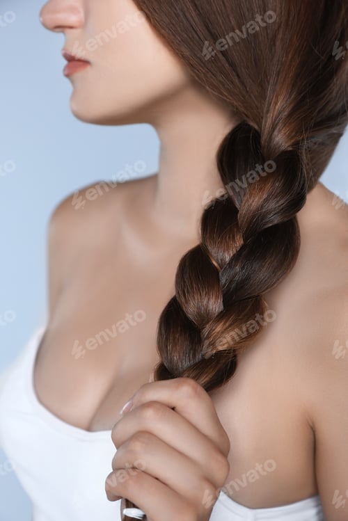 Preview: Young woman with strong healthy braided hair on light blue background, closeup