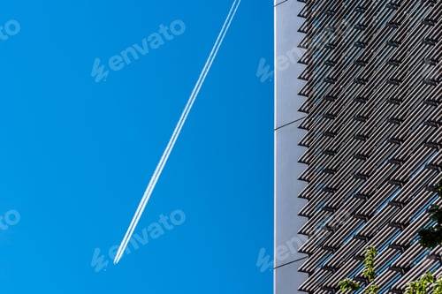 Preview: Closeup shot of a building with white plane trails in a clear blue sky in the background