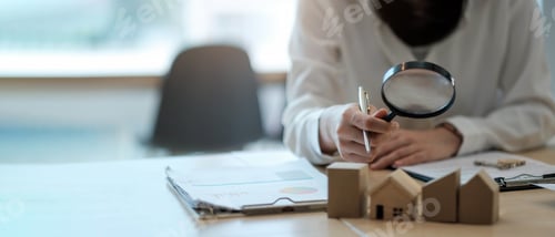 Preview: a woman looks at the house with a magnifying glass and on the table paper and data.
