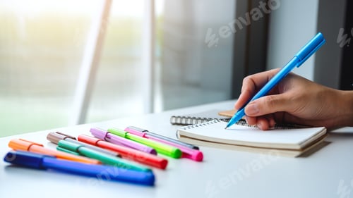 Preview: Closeup image of a woman writing on a blank notebook with colored pens on the table