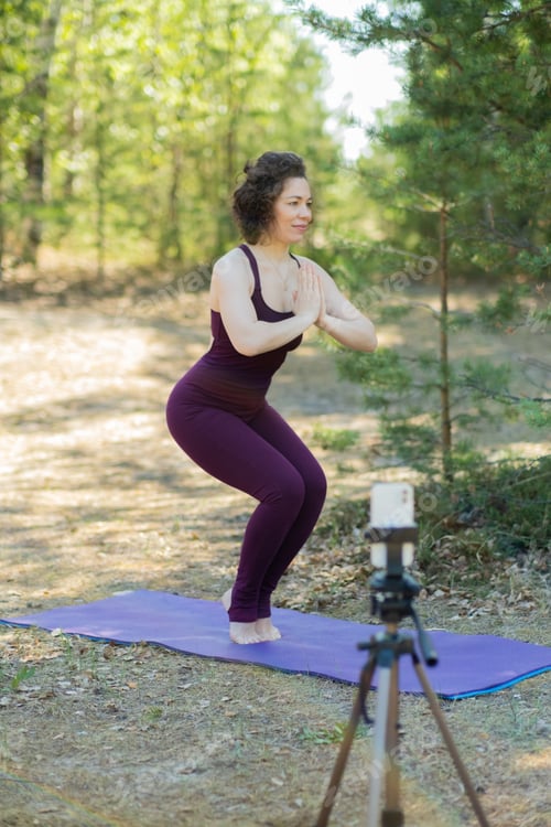 Preview: Young woman doing yoga in nature online using phone and application