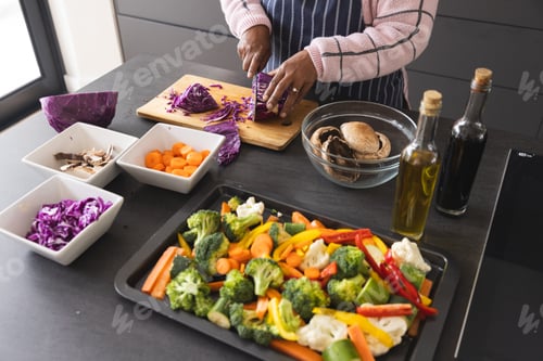 Preview: Senior biracial woman wearing apron and cutting cabbage on table with vegetables in kitchen at home