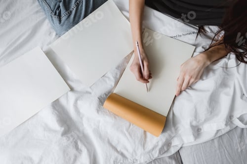 Preview: Woman artist draws in a sketchbook at home in the white bed in comfort and coziness, creativity.