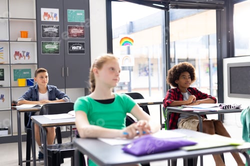 Preview: Diverse pupils sitting at desks listening in classroom, copy space