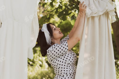 Preview: beautiful young woman in reto style hangs up to dry washed clothes on the street on a summer day