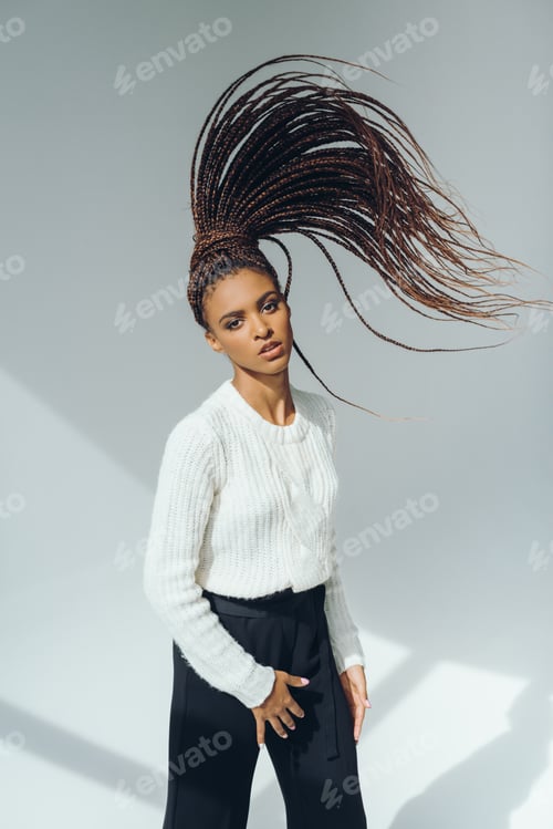 Preview: beautiful african american girl in stylish knitted sweater posing and looking at camera on grey