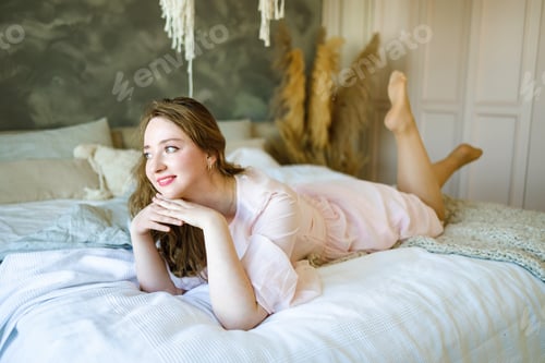 Preview: Smiling young girl relaxing in bed in the morning at modern cozy home.