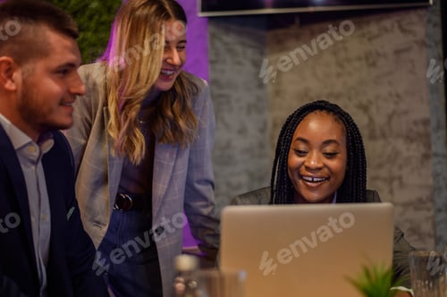 Preview: Cheerful work colleagues working on a laptop while having a meeting in a cafe