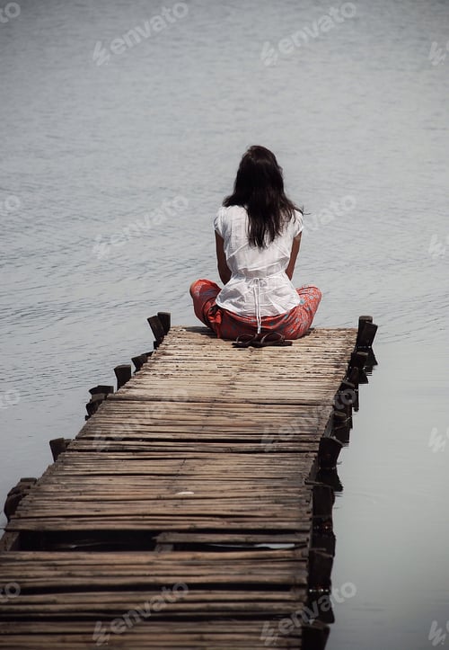 Preview: Mental health is improved through meditation and reflection as a woman sits contemplating on a jetty