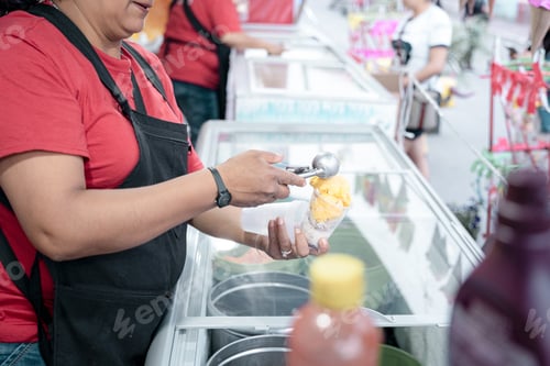 Preview: An Hispanic adult woman is serving some vanilla ice cream balls in a cup in the street