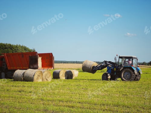 Preview: tractor loading hay bales in a truck across a vast field on summer day