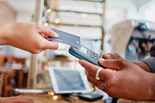 Preview: Closeup of unknown mixed race customer using a wireless credit card machine to pay for her coffee.