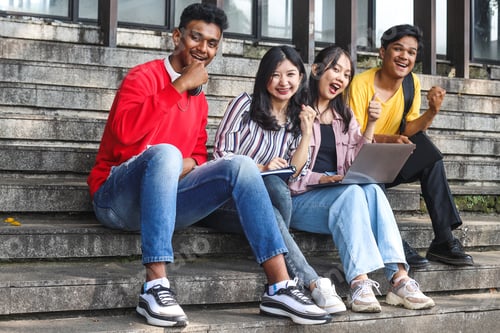 Preview: Young multiethnic college celebrating success while studying on laptop or working on group project