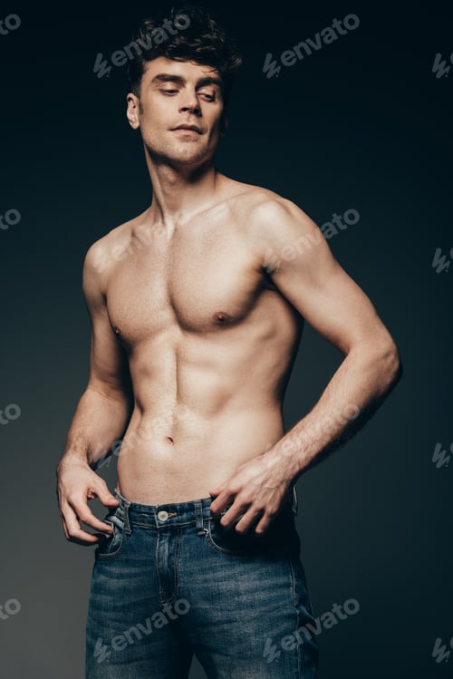 Preview: sexy handsome man in jeans posing isolated on dark grey