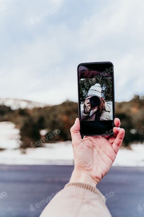 Preview: woman at the mountain taking a self portrait on mobile phone with camera. Winter season
