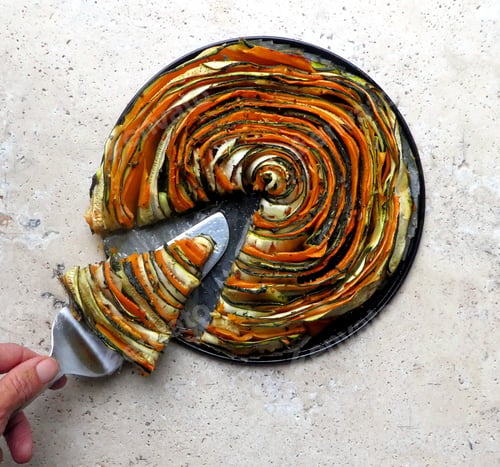 Preview: Overhead view of hand holding slice of healthy food,ratatouille,galette,on stone table