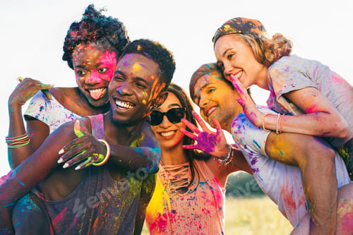 Preview: multicultural happy friends piggybacking together at holi festival