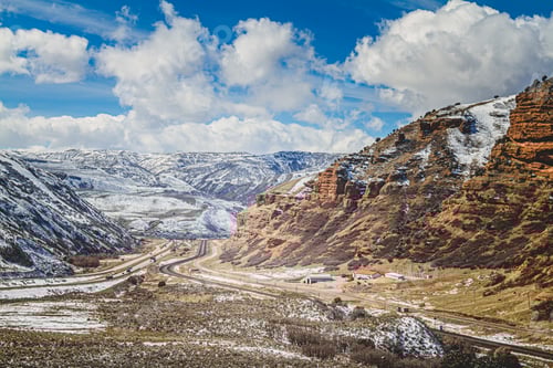 Preview: Scenic winter landscape showcasing snowy mountains, winding road, and fluffy clouds in Wyoming