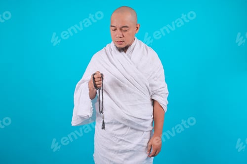 Preview: Muslim Man in Ihram Clothing Holding Prayer Beads, Isolated on Blue Background