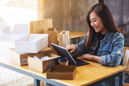 Preview: a young asian woman using tablet pc for online shopping with postal parcel box and shopping bags