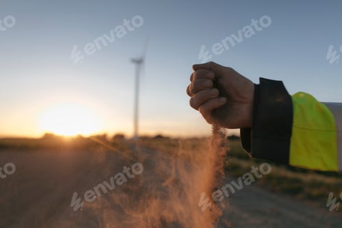 Preview: Close-up of man's hand scattering soil at a wind turbine at sunset