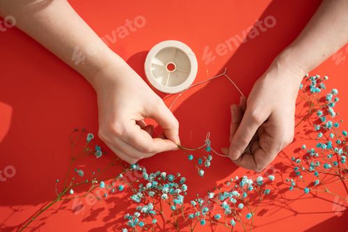 Preview: female hands make a decor of flowers wound on a wire frame in the shape of a heart