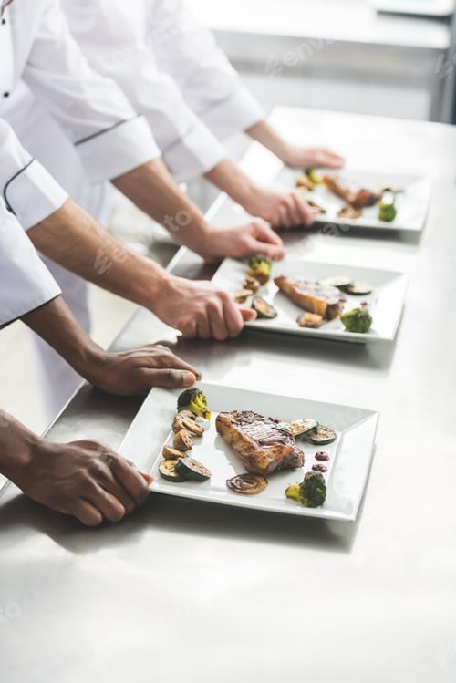 Preview: cropped image of multiethnic chefs with plates with steaks at restaurant kitchen
