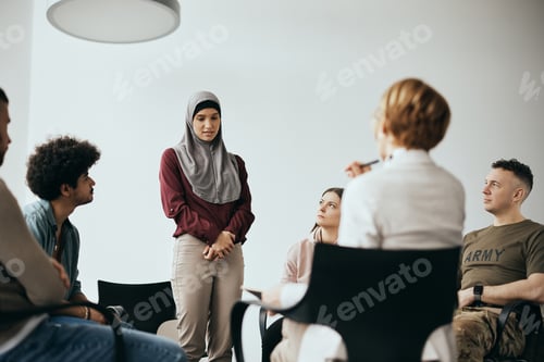 Preview: Young Muslim woman talking about her issues during group therapy meeting at mental health center.