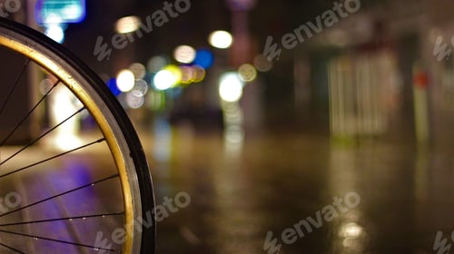 Preview: Closeup of a bicycle wheel in a rainy street at night
