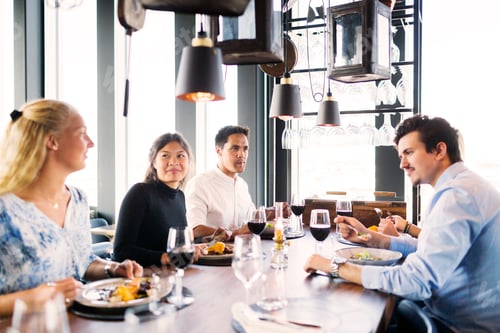 Preview: Happy young friends having meal at table in restaurant